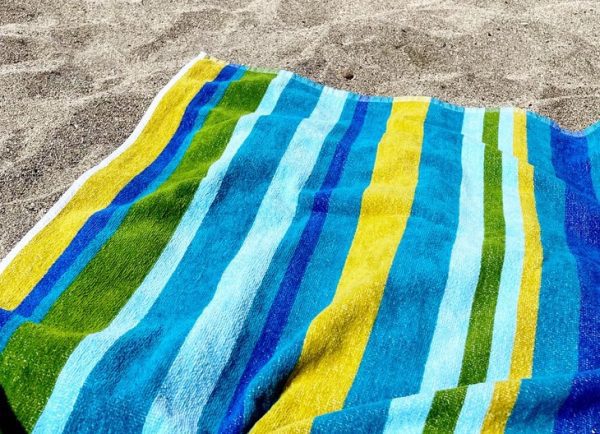 blue striped beach towel on the beach shades of blue and yellow stripes on cotton beach towel sand in background