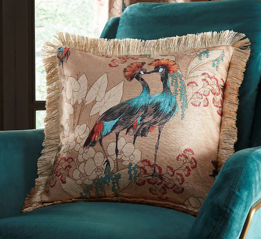 Mariba gold cushion cover with teal botanical print on a gold background, 45x45cm, placed on a teal velvet armchair in a living room